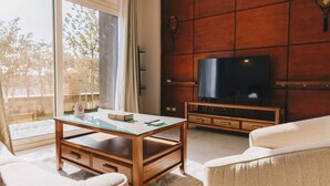 A living room with a glass coffee table, a sofa, a TV on a wooden stand, and a sliding glass door leading to an outdoor area. - The Suite, Palm Hills - V702 (New Cairo City)