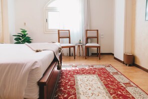 Ein Schlafzimmer mit einem Bett, zwei Stühlen, einem kleinen Tisch, einer Pflanze und einem Fenster.