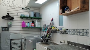 A compact kitchen with a washing machine, drying rack, and various kitchen utensils on shelves.