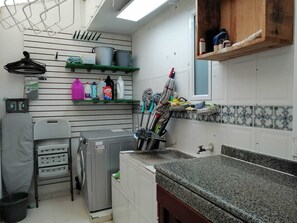 Cocina compacta con lavadora, tendedero y diferentes utensilios de cocina en estantes.