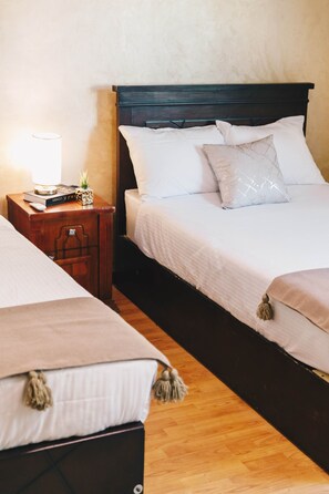 Ein Hotelzimmer mit Holzboden, einem Bett mit weißer Bettwäsche, einem Nachttisch mit Lampe und einem kleinen dekorativen Gegenstand.