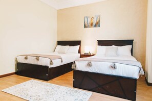 A hotel room with two beds, a wooden floor, a painting on the wall, and a small bedside table with a lamp. - Maple and Moon Suite - Comfort & Elegance Stay 3 (New Cairo City)