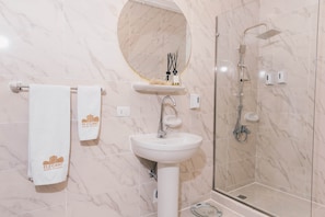 Ein Badezimmer mit Marmorwand, einem Waschbecken, einem Spiegel, einer Dusche und zwei Handtüchern mit einem Logo.