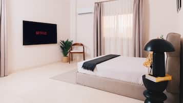 A modern bedroom with a bed, a TV mounted on the wall, a potted plant, and a lamp.