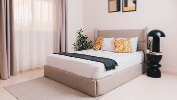 A bedroom with a bed, curtains, a plant, a lamp, and artwork on the wall.