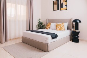 Ein Schlafzimmer mit Bett, Vorhängen, einer Pflanze, einer Lampe und Bildern an der Wand.