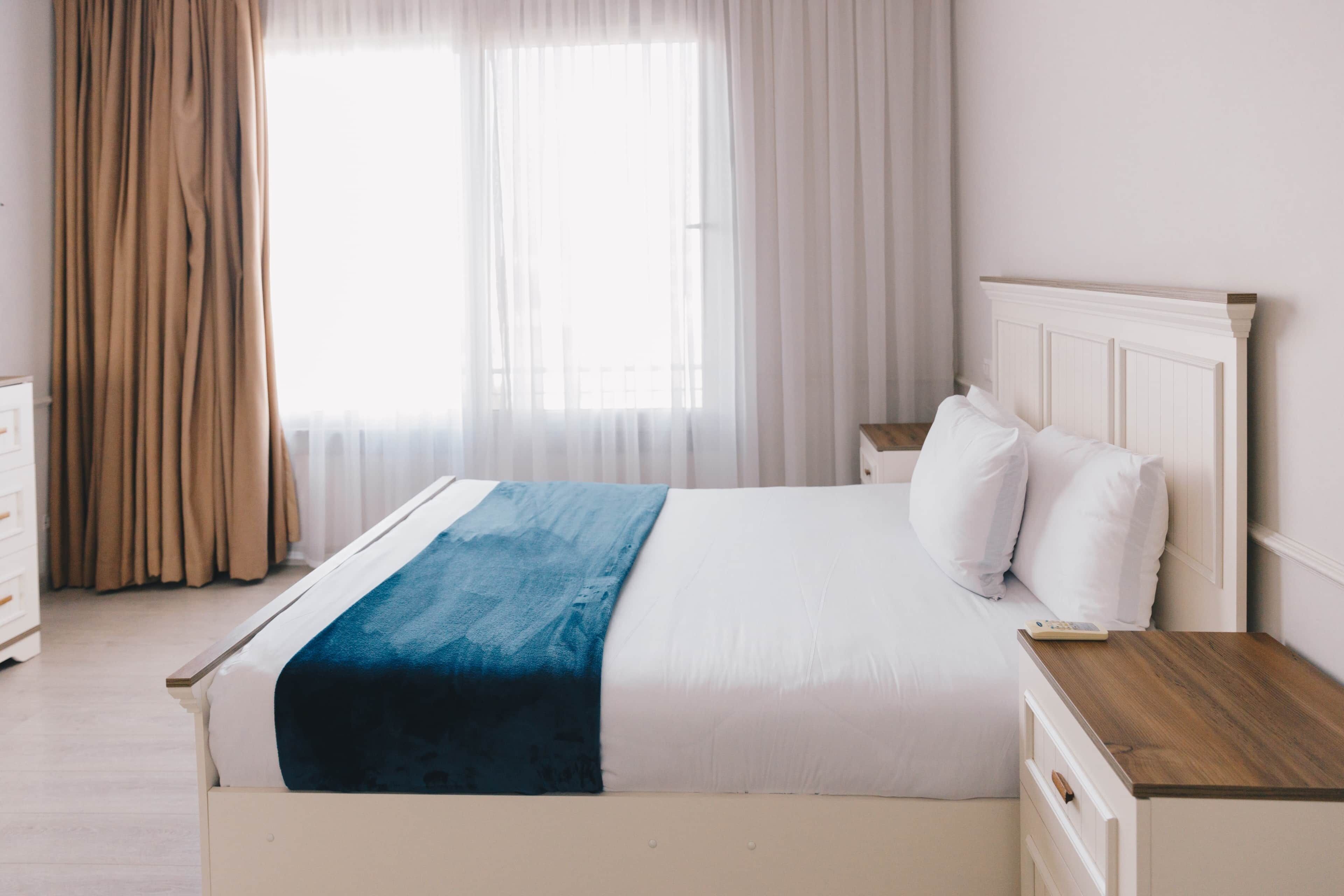 A bed with a white headboard, a wooden bedside table, and a blue blanket.