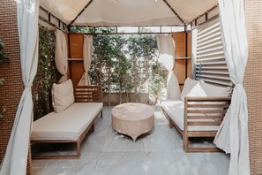 A covered outdoor seating area with two sofas and a round table, surrounded by brick walls and a view of greenery. - The Suite, Palm Hills - VG802 (New Cairo City)