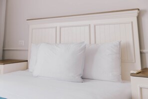 Cama com roupa de cama branca e cabeceira de madeira.