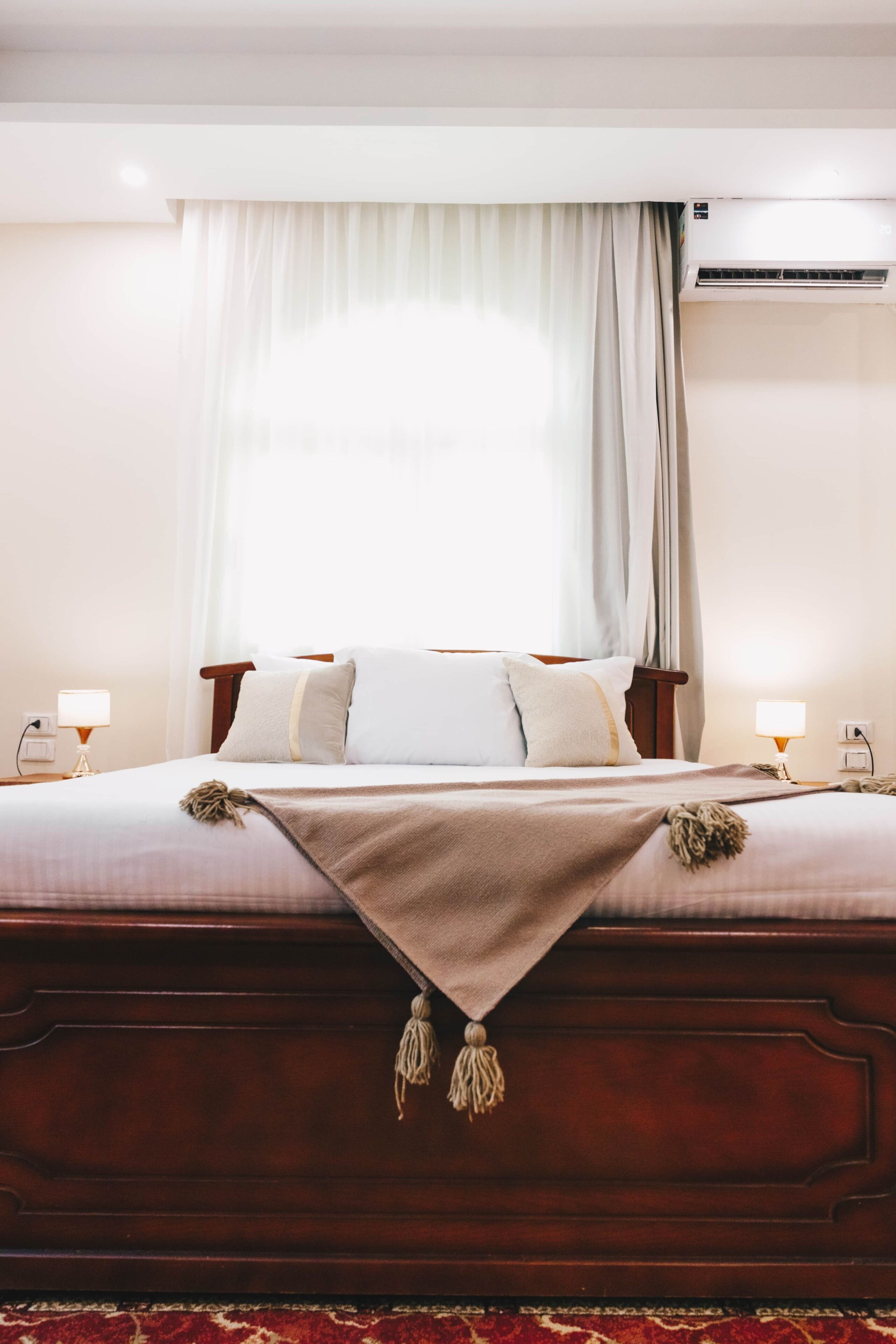 Une chambre d’hôtel avec un grand lit, une table de chevet, une lampe et une fenêtre avec des rideaux.