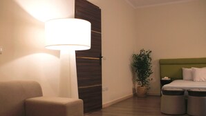 Een hotelkamer met een bed, nachtkastje, lamp, stoel en een plant in pot.