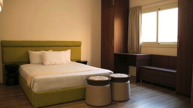Een slaapkamer met een bed, nachtkastjes, een bankje en een kledingkast.