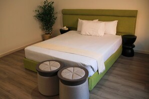 Ein ordentlich bezogenes Bett mit grünem Kopfteil, zwei Nachttischen und zwei runden Hocker in einem modernen Hotelzimmer.
