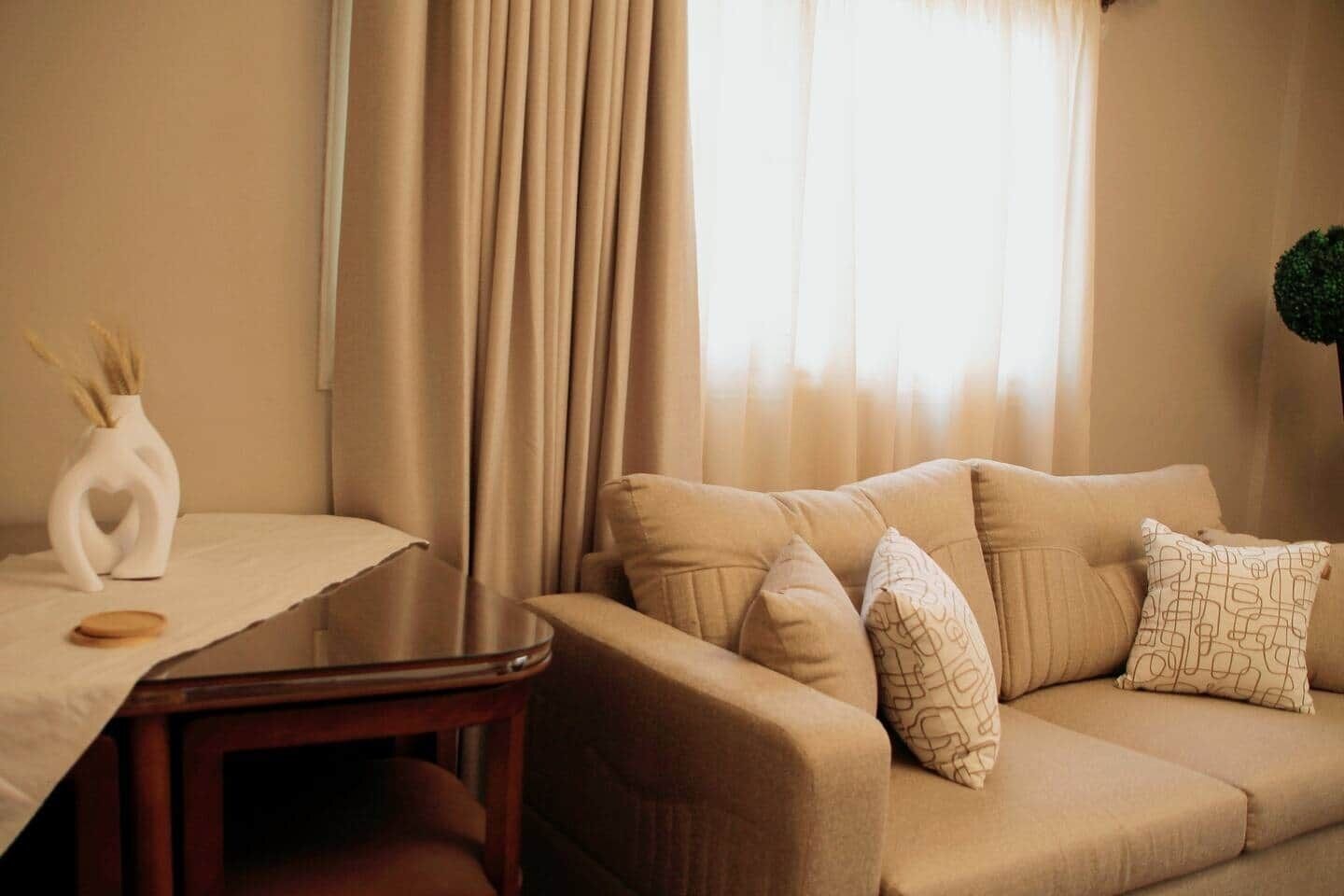 Una sala de estar con un sofá color beige, una mesa de centro de madera y un jarrón con cañas.