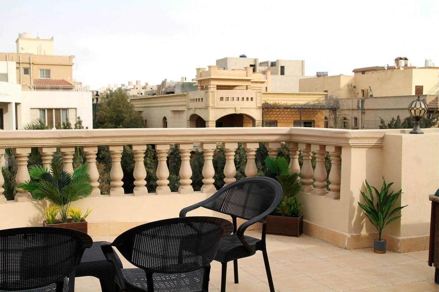 Una terraza en la azotea con dos sillas negras, barandilla y plantas en macetas.