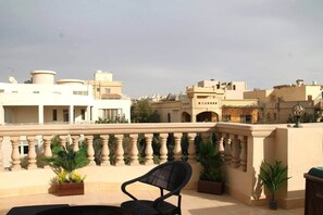 A rooftop terrace with a black chair, potted plants, and a balustrade. - Luxury 2BR Rooftop Apartment with Jacuzzi (New Cairo City)
