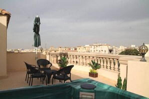 A terrace with a table and chairs, a potted plant, and a view of buildings. - Luxury 2BR Rooftop Apartment with Jacuzzi (New Cairo City)