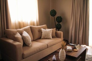A beige sofa with patterned pillows, a wooden coffee table, and a decorative vase. - Luxury 2BR Rooftop Apartment with Jacuzzi (New Cairo City)