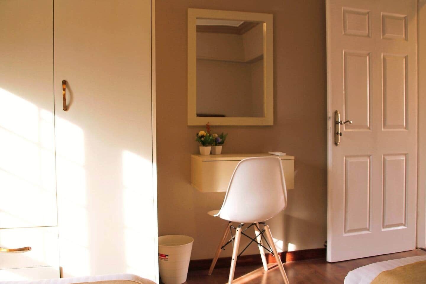 A room with a bed, a white chair, a small table with a plant, and a door.