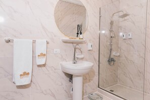Ein Badezimmer mit Marmorwand, einem Waschbecken, einem Spiegel, einer Dusche und zwei Handtüchern mit einem Logo.