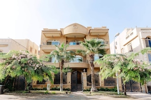 A multi-story building with balconies, a central entrance, and palm trees in the foreground. - Maple and Moon Suite - Comfort & Elegance Stay 6 (New Cairo City)