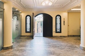 A hallway with a marble floor, a black door, and two arched windows with decorative frames. - Maple and Moon Suite - Comfort & Elegance Stay 6 (New Cairo City)