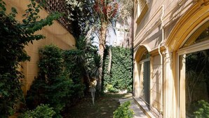 A narrow courtyard with dense foliage, a palm tree, and a building with arched windows. - Maple and Moon Suite - Comfort & Elegance Stay 6 (New Cairo City)