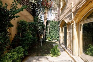 A narrow courtyard with dense foliage, a palm tree, and a building with arched windows. - Maple and Moon Suite - Comfort & Elegance Stay 6 (New Cairo City)