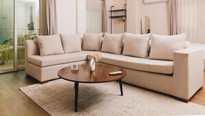 Una sala moderna con un sofá seccional color beige, una mesa de centro redonda y un ventanal de vidrio que da a un balcón.