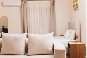A hotel room with a bed, a bedside table with a lamp, a window with curtains, and a wall-mounted air conditioner. - VIOLA Near Waterway  - 42 (New Cairo City)