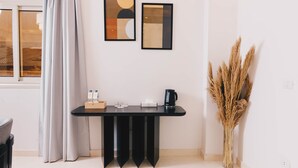 Une pièce moderne avec une table noire, deux œuvres d’art abstraites encadrées, un vase contenant des plantes séchées et une fenêtre avec des rideaux.