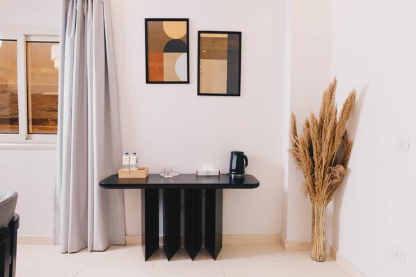 Una habitación moderna con una mesa negra, dos cuadros abstractos enmarcados, un jarrón con plantas secas y una ventana con cortinas.