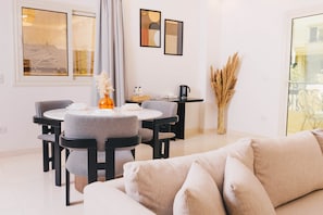 A modern living room with a round dining table, grey upholstered chairs, a beige sofa, and a vase with dried plants. - VIOLA Near Waterway  - 01 (New Cairo City)