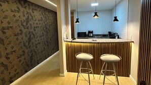 Cocina moderna con una isla central, dos taburetes de bar, iluminación colgante y un papel tapiz estampado.