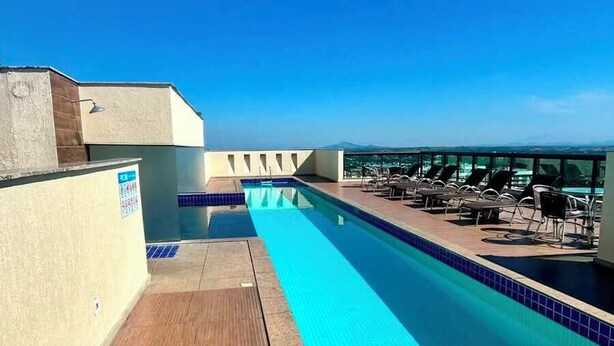 Una piscina en la azotea con vistas despejadas del paisaje urbano, rodeada de sillones de descanso.