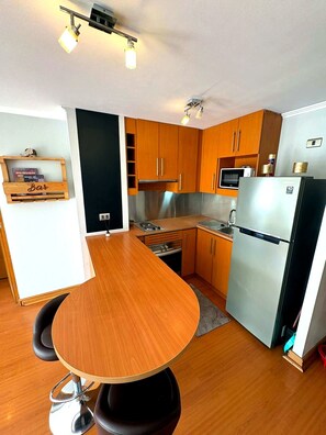 Eine kompakte Küche mit Holzschränken, einem Edelstahlkühlschrank, einer Mikrowelle und einer Barbereich-Ausstattung.