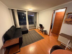 Ein kompakter Wohnraum mit einer Couch, einem kleinen Fernseher, einem Holzschrank und einem Balkon mit Vorhängen.