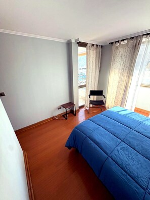 Ein Schlafzimmer mit einem Bett, einem Sessel, einem kleinen Tisch und einem Fenster mit Vorhängen.