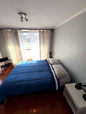 Ein Schlafzimmer mit Bett, Stuhl, Schreibtisch und einem fenster mit Vorhängen.