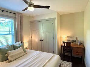 Ein Schlafzimmer mit Bett, Schreibtisch, Stuhl, Deckenventilator und Tür.