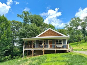 Eine Holzhütte mit Veranda, umgeben von Bäumen und einem klaren Himmel.