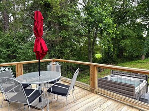 Una terraza de madera con una mesa redonda y sillas, una sombrilla roja y un jacuzzi.