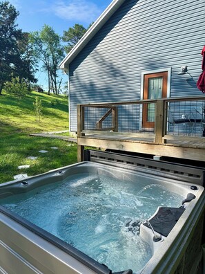 Un jacuzzi frente a una casa con terraza de madera y barandilla.