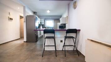 Una cocina moderna con una isla central, dos taburetes de bar, un refrigerador y un reloj en la pared.