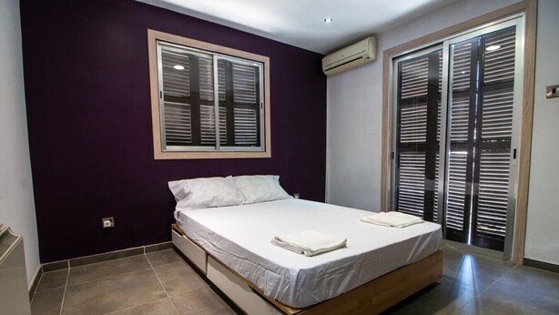 Ein Schlafzimmer mit Bett, Fenster, einer Jalousie und einer Klimaanlage.