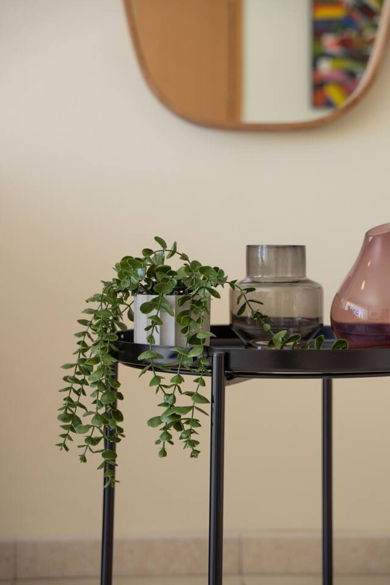 Een tafeltje met een potplant, een glazen vaas en een roze vaas.
