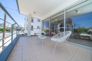 A balcony with a glass door, white chairs, a small table, and a potted plant.