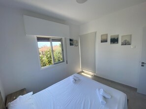 Een slaapkamer met een groot bed, een raam met zonwering en een deur.