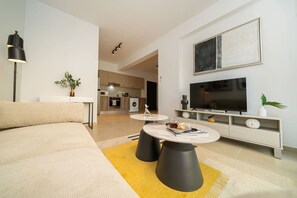 Ein modernes Wohnzimmer mit einer Couch, einem Couchtisch, einem Fernseher und einer Küche im Hintergrund.
