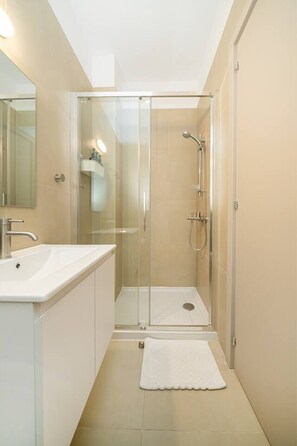 Une salle de bain moderne avec une douche à parois de verre, un lavabo blanc et un miroir.